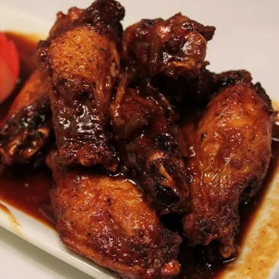 Close-up of several Caribbean-style chicken wings coated in a rich, dark, glossy sauce on a white plate.