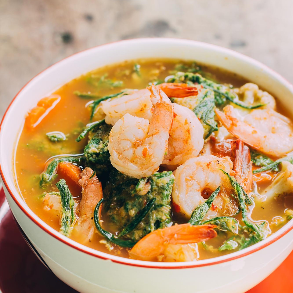 A vibrant Caribbean shrimp and vegetable stew in a white bowl with a red rim.
